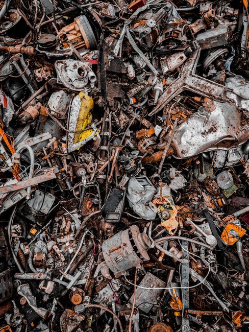 A large pile of discarded automotive parts and metal scraps, including engine components, gears, wires, and various mechanical debris, all exhibiting rusted, corroded, and weathered textures in shades of brown, gray, and black. The debris is haphazardly stacked and spread across a flat surface, with some items overlapping and tangling. The environment appears to be an outdoor scrapyard or waste disposal site, with no visible background or greenery, focusing solely on the dense collection of metallic waste. The lighting is natural and diffuse, highlighting the irregular surfaces and textures of the metal objects. This scene illustrates the type of material typically encountered in the collection, transportation, or disposal of bulky automotive waste, which waste disposal services like Waste Disposal Croydon manage as part of confidential or environmentally responsible rubbish removal processes involving on-site clearance of scrap materials.